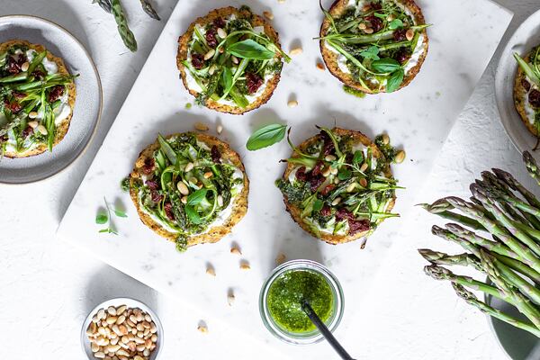 Hotové pizzy ozdobte bylinkovým pestem, sušenými rajčaty a hlavičkami chřestu.